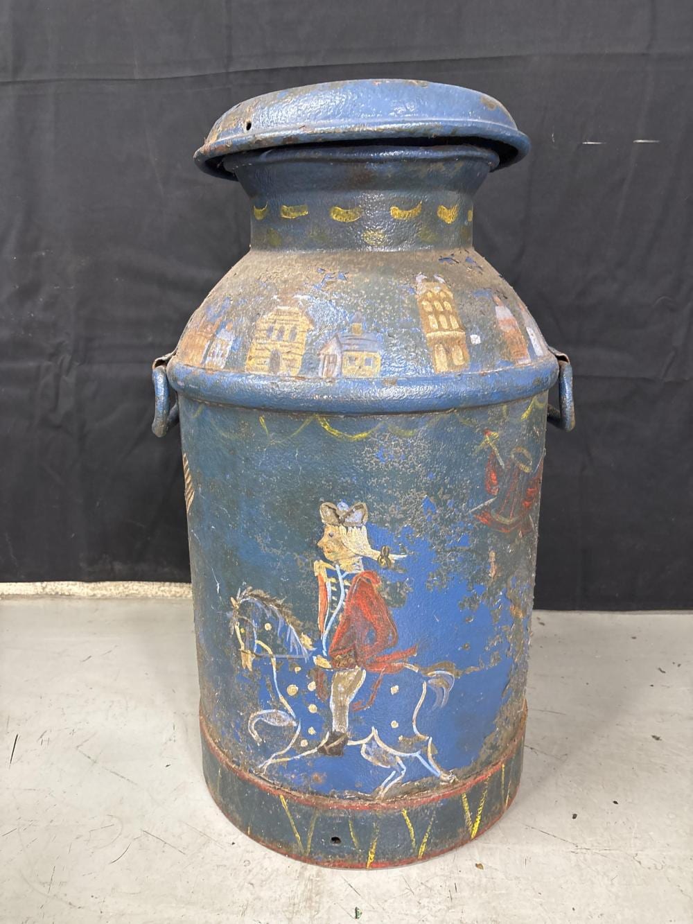 Blue metal milk can with lid and patriotic colonial-style painted figures and buildings on the sides.