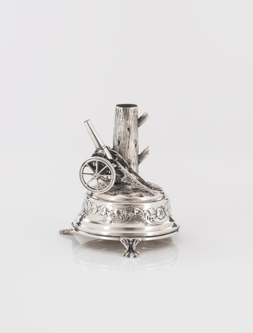 Silver-colored decorative toothpick holder with an upright cannon-like handle, a wheel motif, and etched floral designs on a round base.