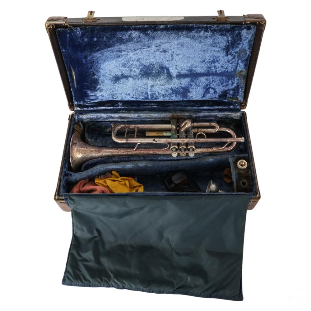 Vintage brass trumpet resting in an open blue-lined case with cleaning cloths and accessories inside.