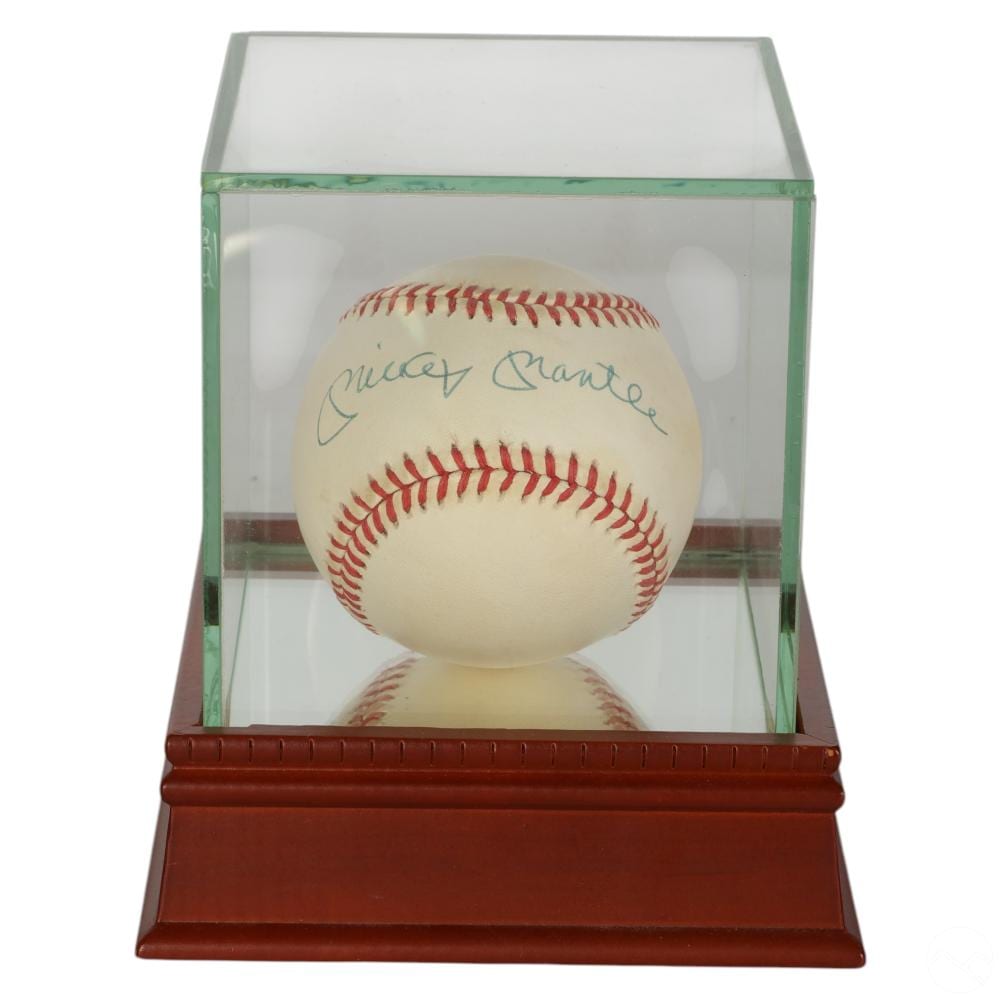 Baseball with red stitching and a blue autograph, displayed inside a clear case with green frame and brown base.
