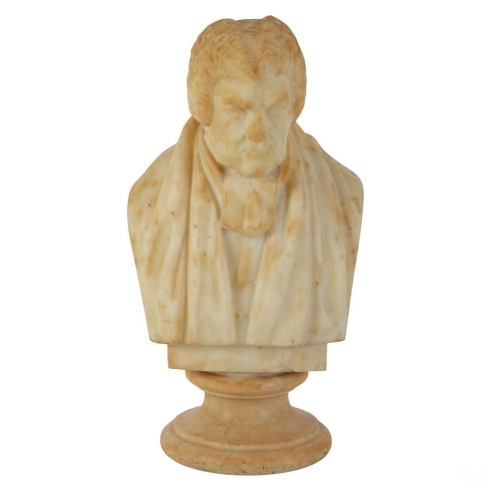 Carved stone bust of an elderly man with white hair, wearing a draped robe, shown on a pedestal against a white background.