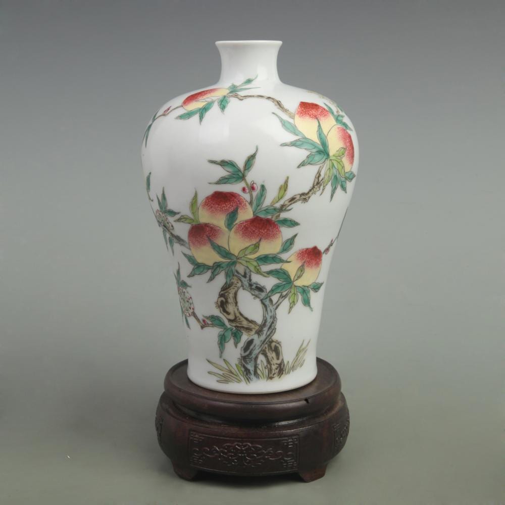White porcelain vase with a narrow neck and floral decoration featuring peach-like flowers and green leaves, shown on a dark wooden stand.
