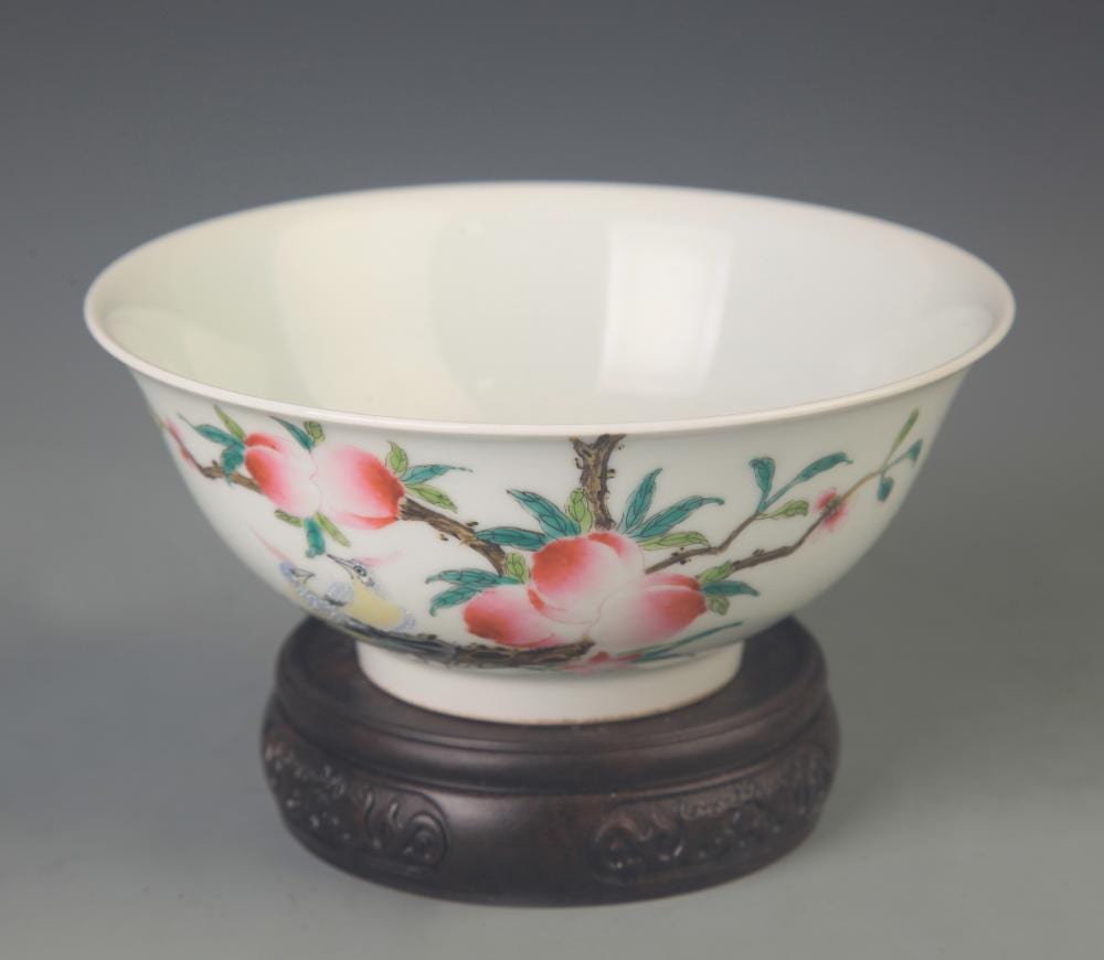 Porcelain bowl with pink peony-like flowers and green leaves on the exterior, shown on a dark wooden stand against a gray background.