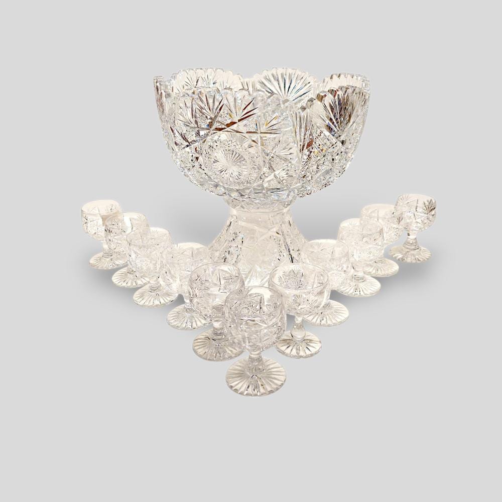 Cut-glass punch bowl with multiple small matching cups, arranged around the bowl on a light background.