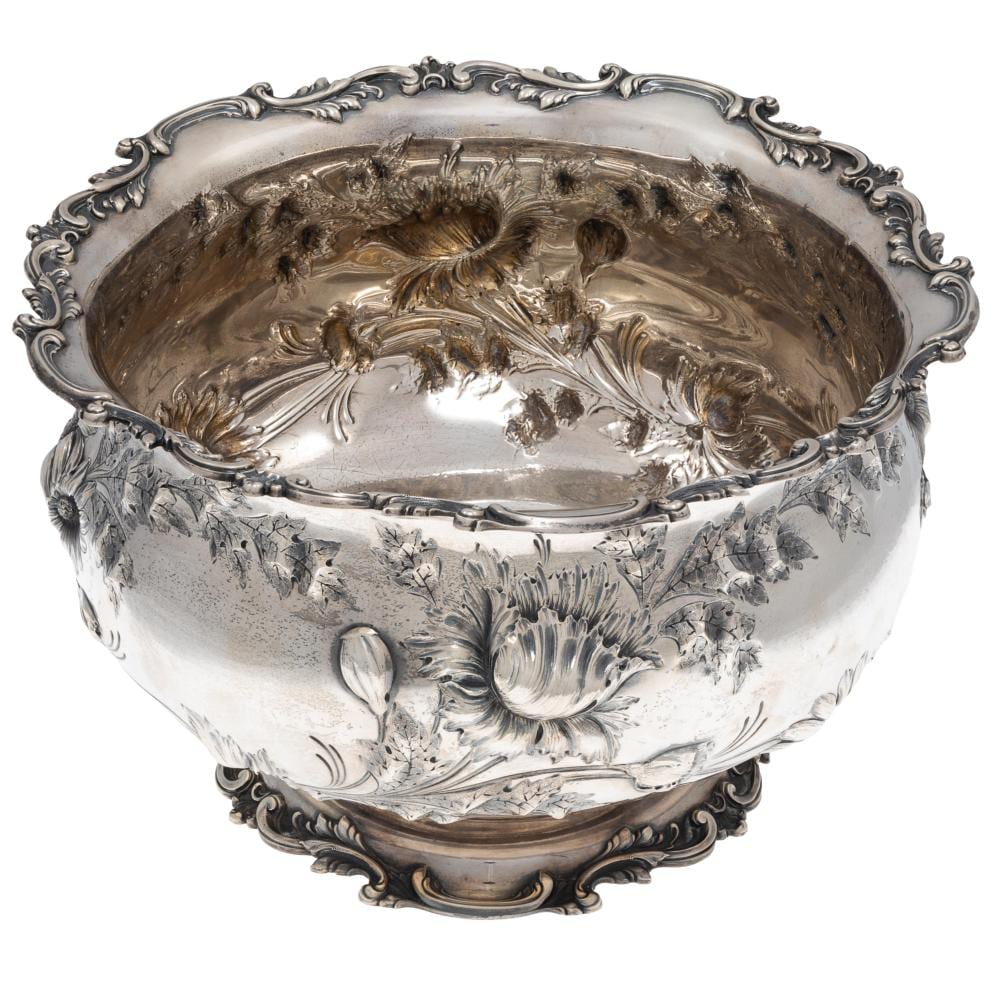 Close-up of an ornate silver bowl with decorative floral engravings and a scalloped rim, shown on a white background.