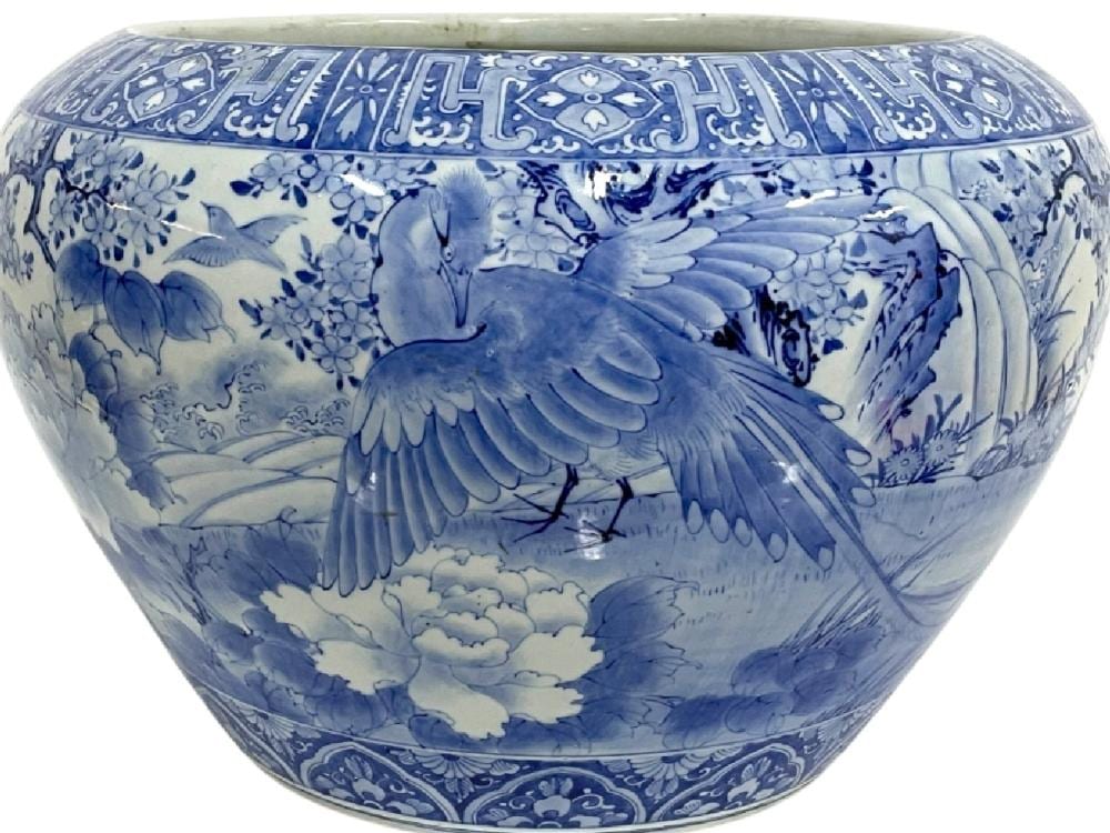 Blue-and-white ceramic fishbowl planter with painted cranes, birds, and floral motifs, shown in close-up.