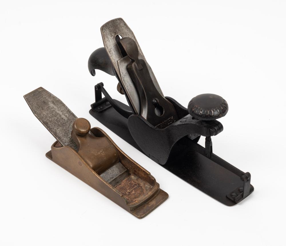 Two vintage hand woodworking planes shown side by side on a white background: a black metal compass plane and a brown brass plane.