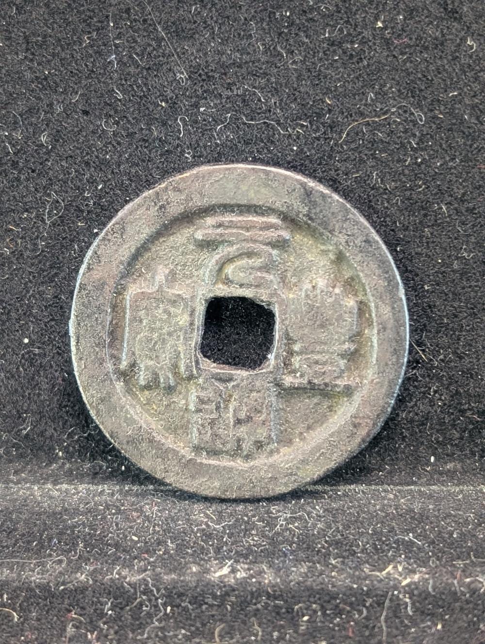 Close-up of a circular metal coin with a square center hole, shown on a dark textured background.