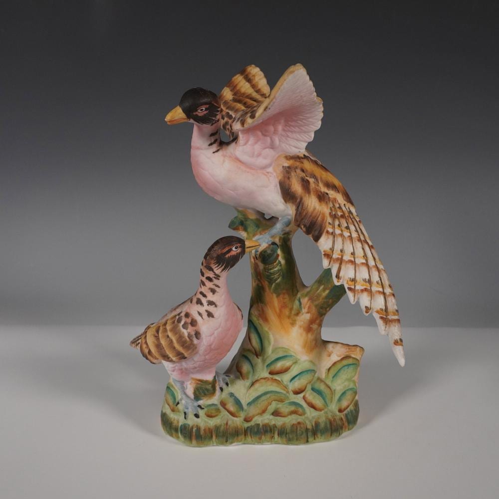 Porcelain figurine of two songbirds perched on a painted tree stump, with one bird in flight over the top wing.