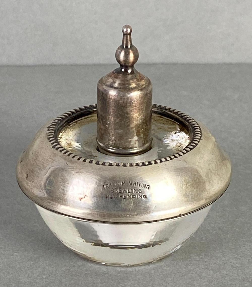Silver desk lighter with a round base and perforated rim, with a small capped spout on top.
