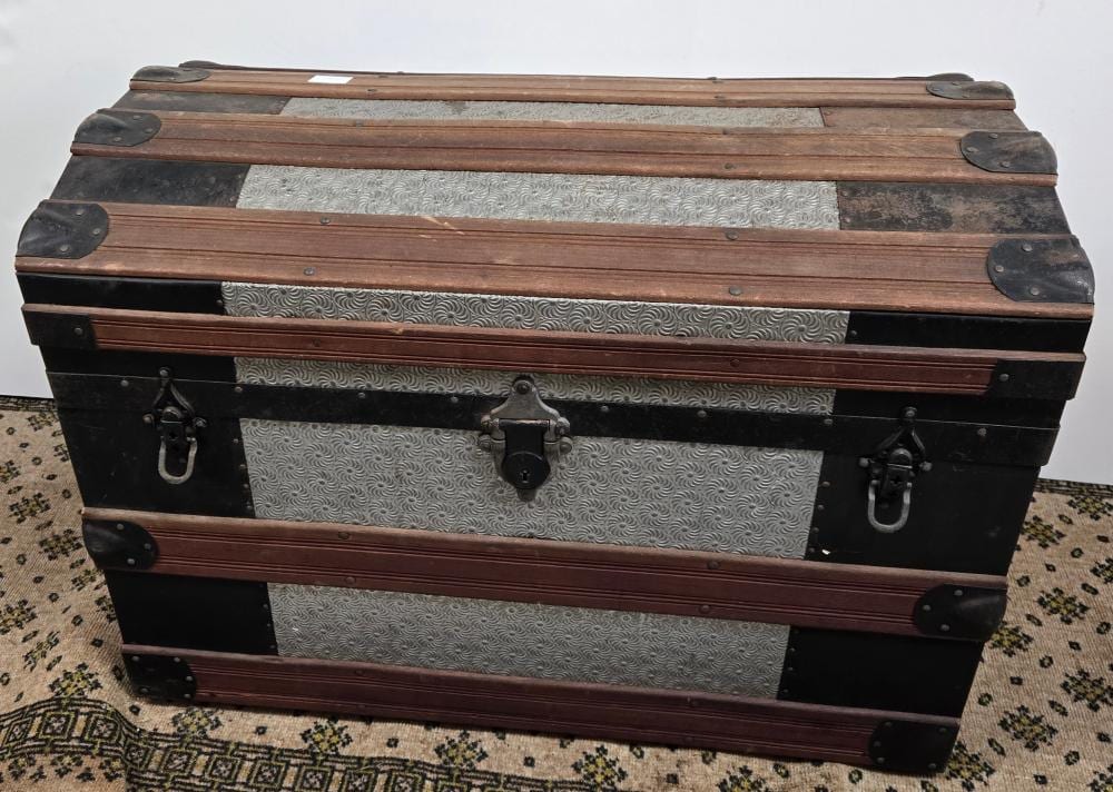 Vintage wooden dome-top trunk with black metal corner brackets, latches, and a textured patterned interior panel.