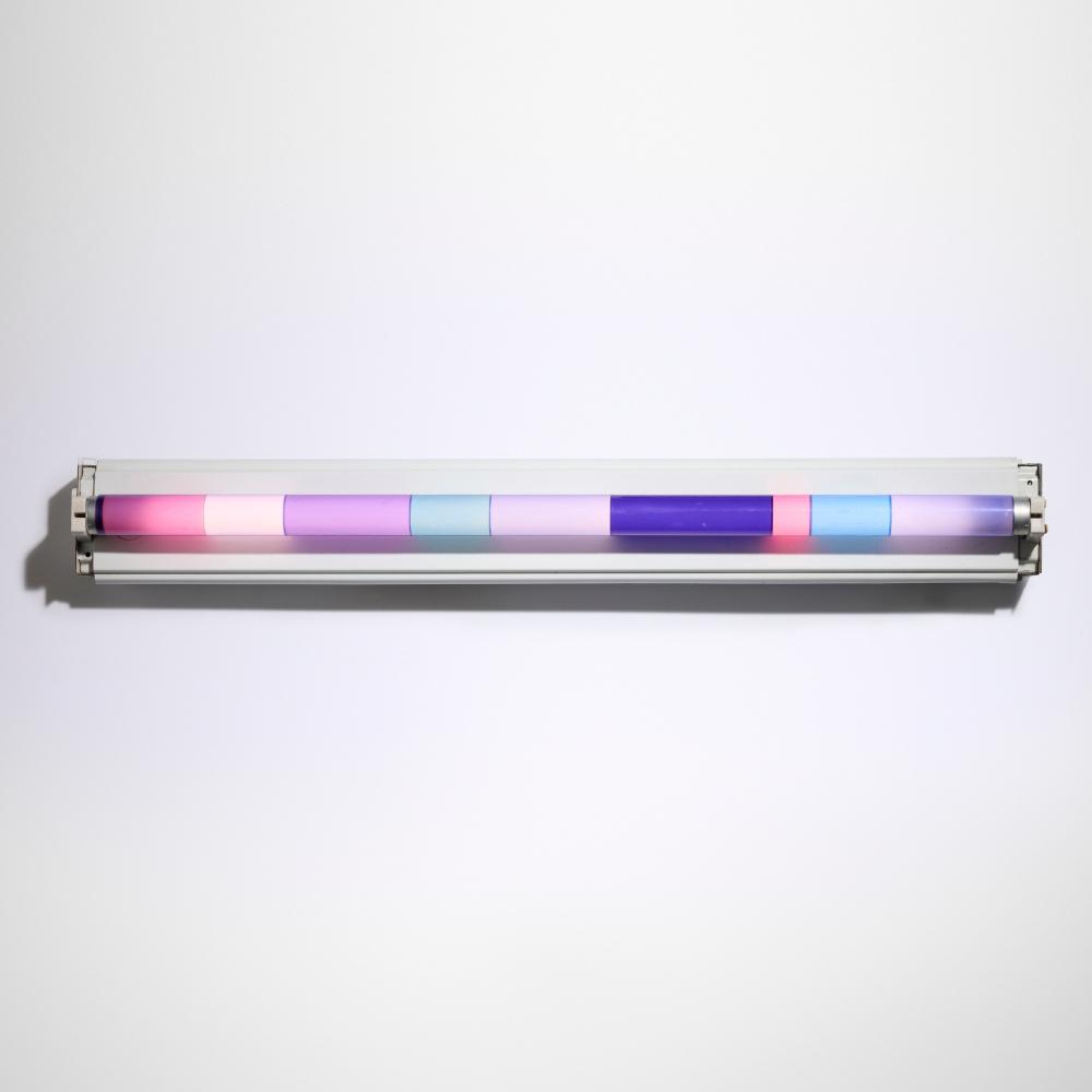 Horizontal art light or display device with glowing segmented bands in pink, purple, and blue mounted on a white wall.