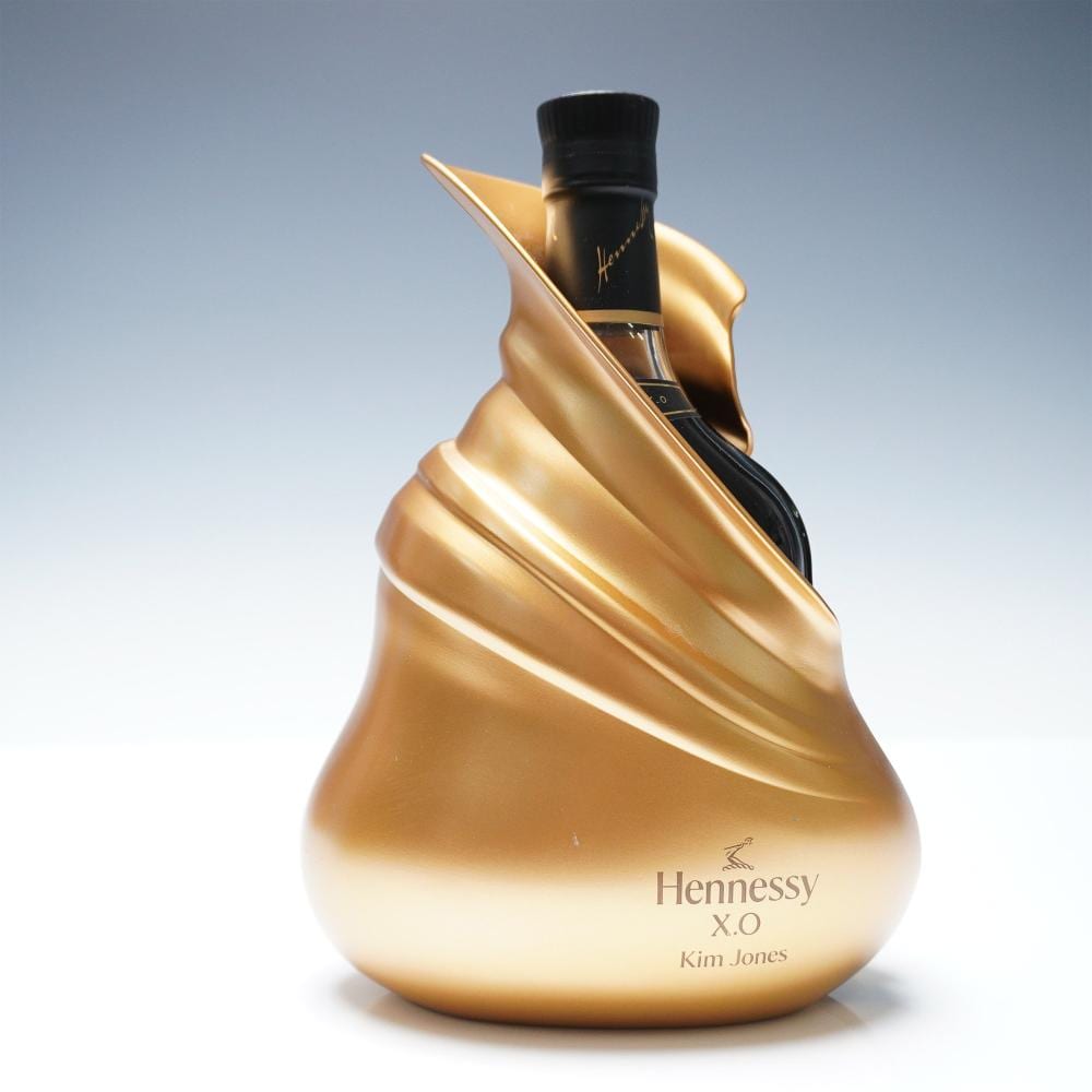 Gold decorative bottle with a black cap and neck, shown against a light background; label text reads “Hennessy X.O” and “Kim Jones.”