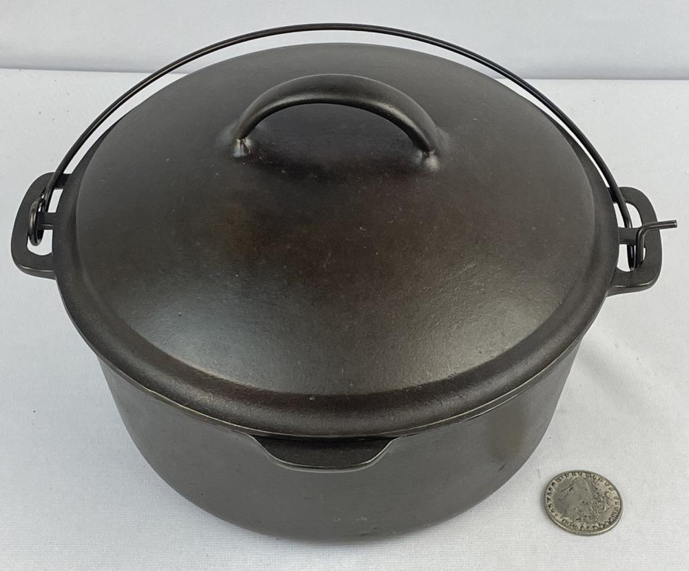 Close-up of a black cast iron dutch oven with a matching lid and side handles, shown with a small coin for size comparison.