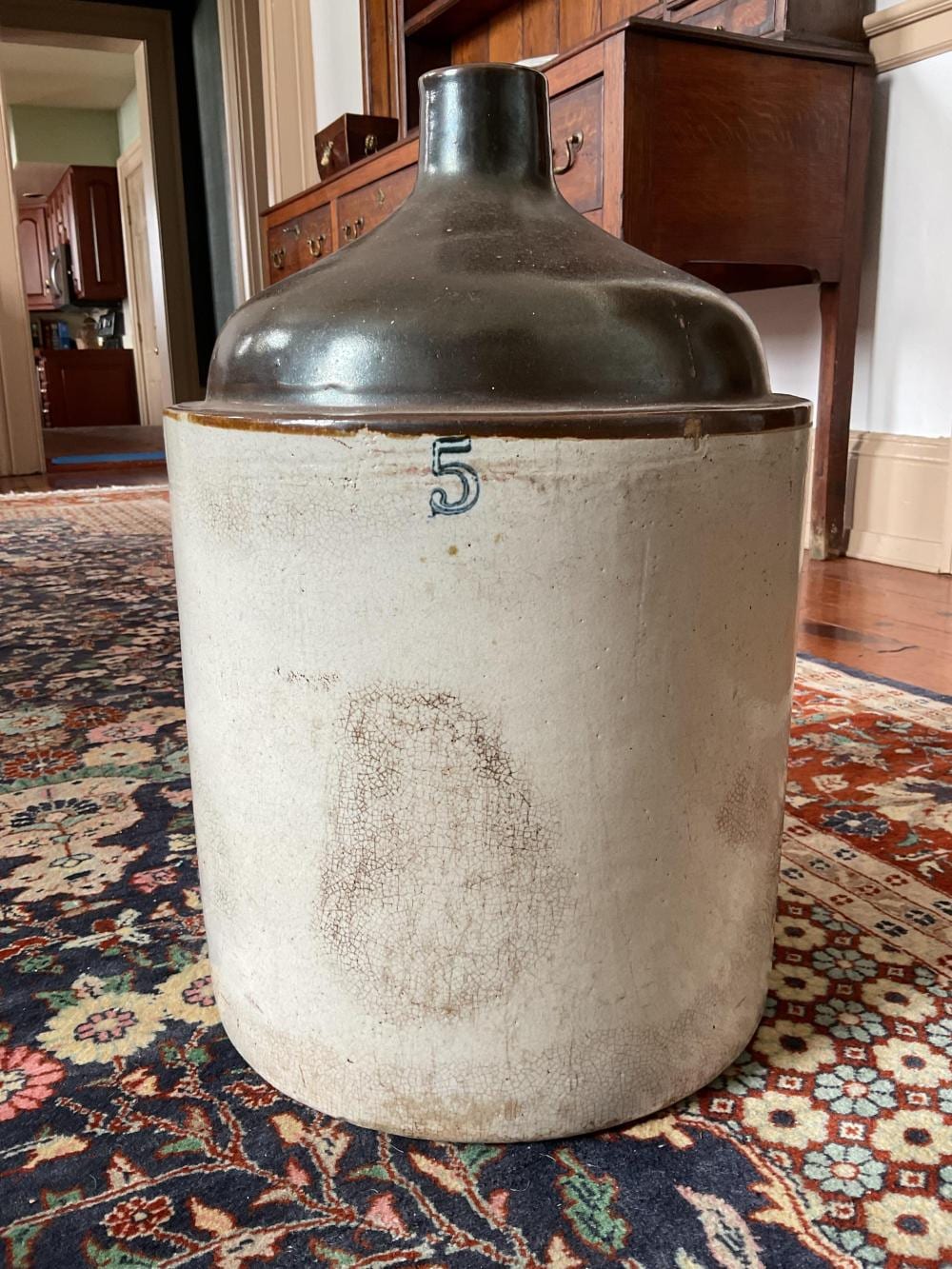 Large white stoneware whisky jug with a dark gray metal neck and a blue numeral “5” on the body, shown indoors.