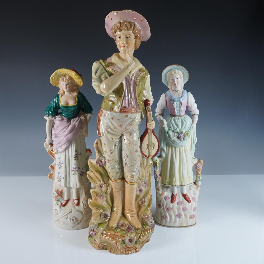 Three porcelain figurines of people in colorful clothing and hats, standing on a light background.