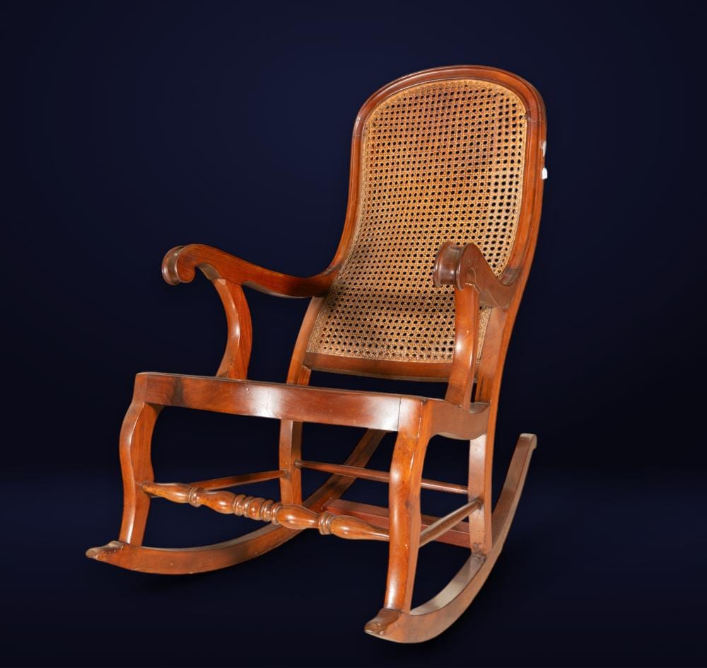 Antique-style wooden rocking chair with a curved back and woven cane seat against a dark background.
