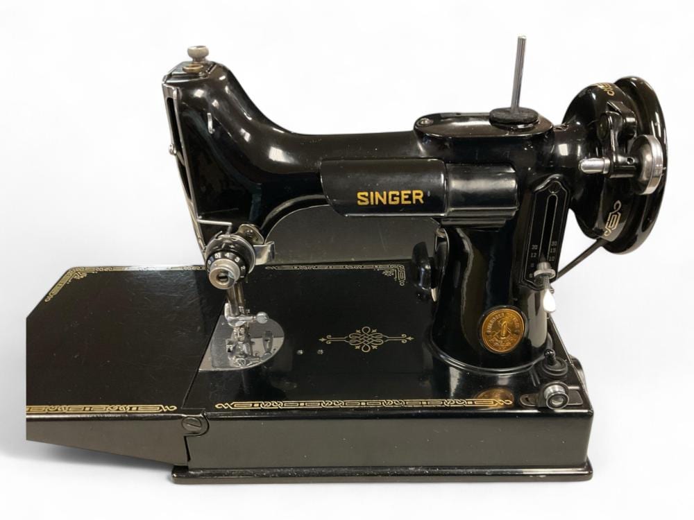 Black Singer Featherweight-style sewing machine with a hand crank, foot pedal base, and gold “SINGER” label on the body.