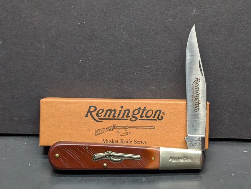 Remington pocket knife with a stainless steel blade open, showing a maroon/brown handle and a Remington logo on the box backing card.