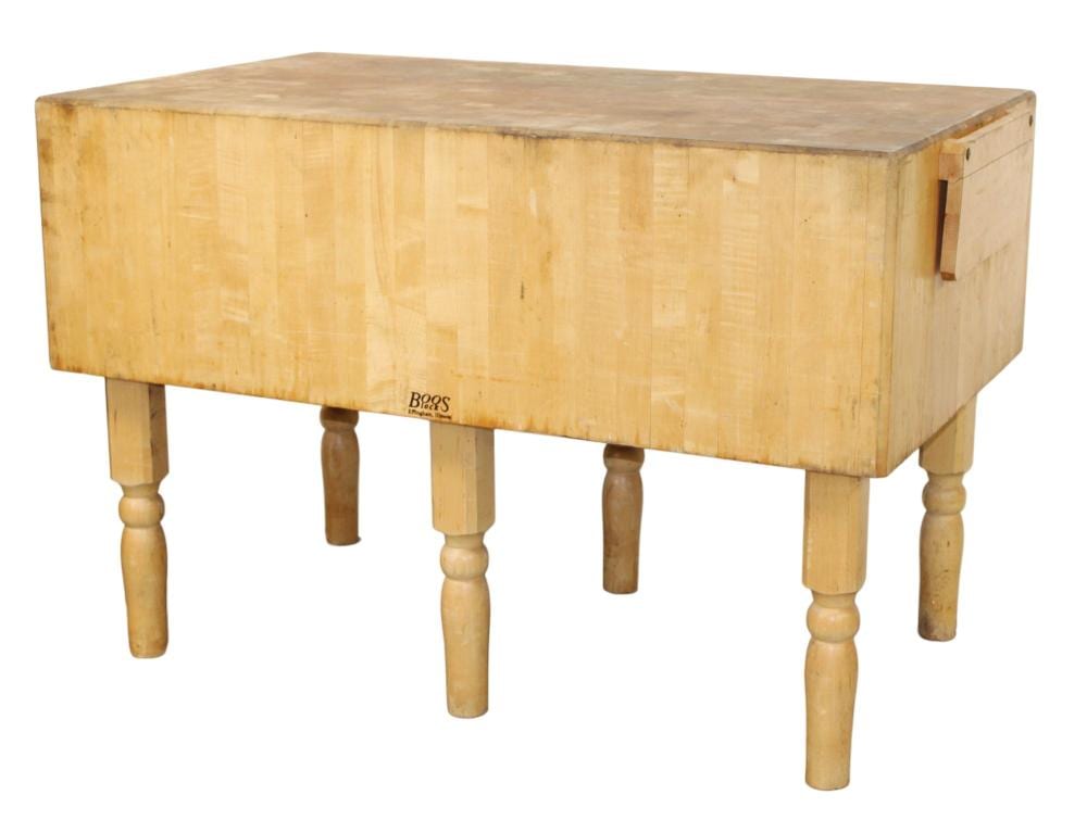 Rectangular wooden butcher block on four turned legs, with a corner cutout and brand label on the front edge.