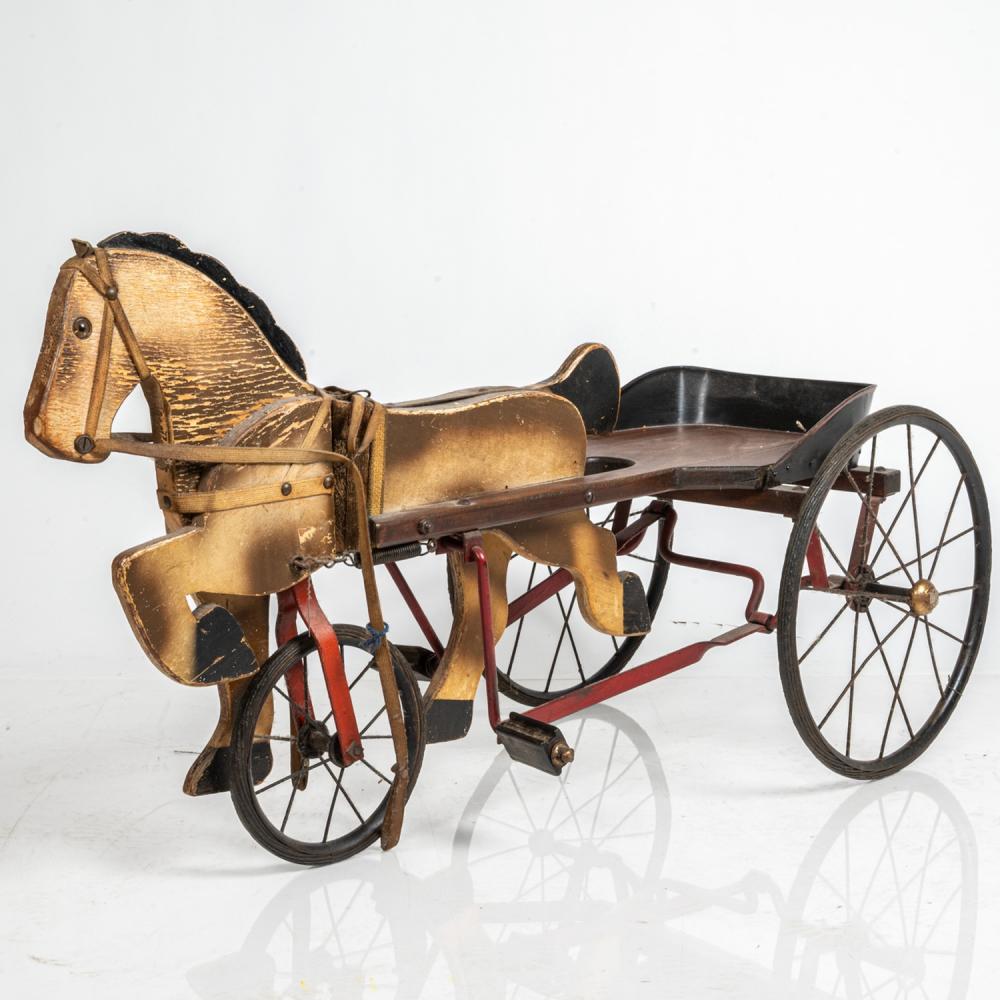 Vintage wooden peddle tricycle shaped like a horse with a carriage-style seat, black wheels, and a curved handle.