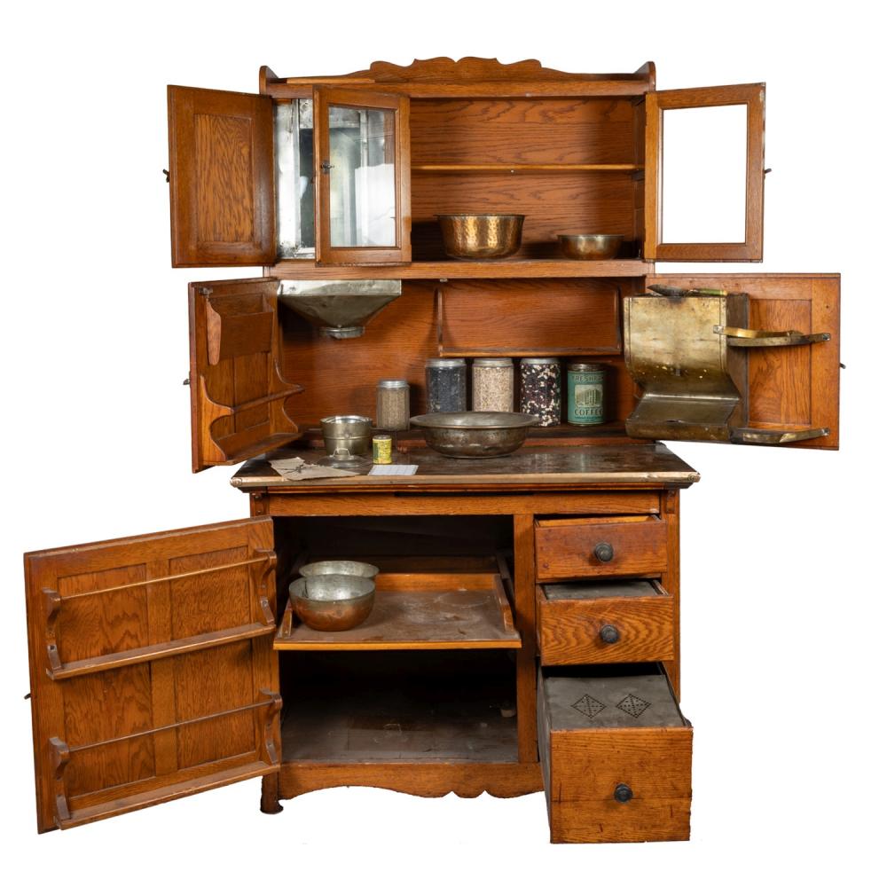 Wooden Hoosier-style kitchen cabinet with open compartments, shelves, and drawers; metal pans and storage containers are visible inside and on top.