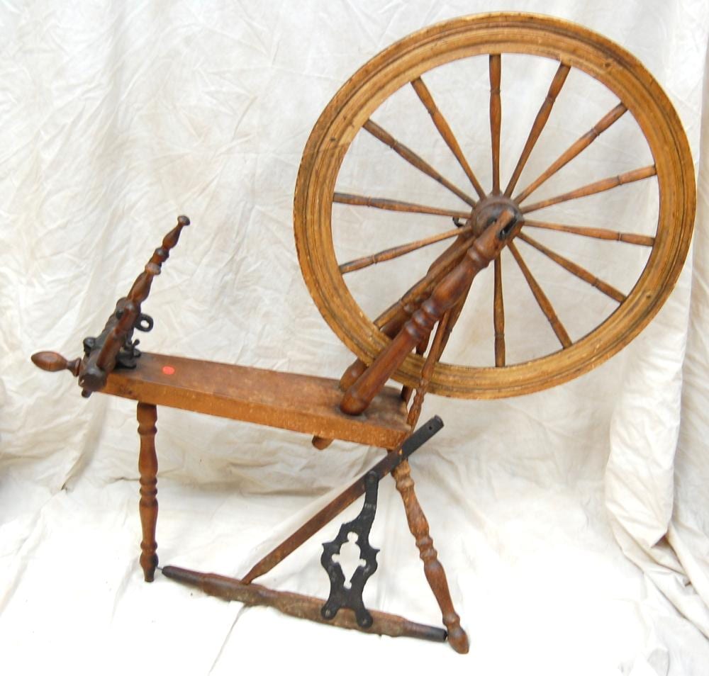 Antique wooden spinning wheel with a large wheel and upright spindle on a white background.