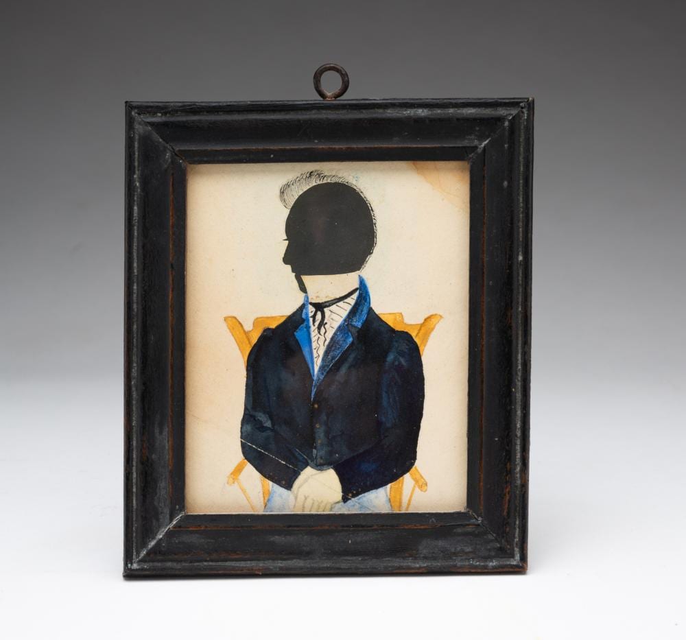 Framed miniature silhouette of a man in profile, wearing a dark blue suit and white shirt with a light orange background behind him.