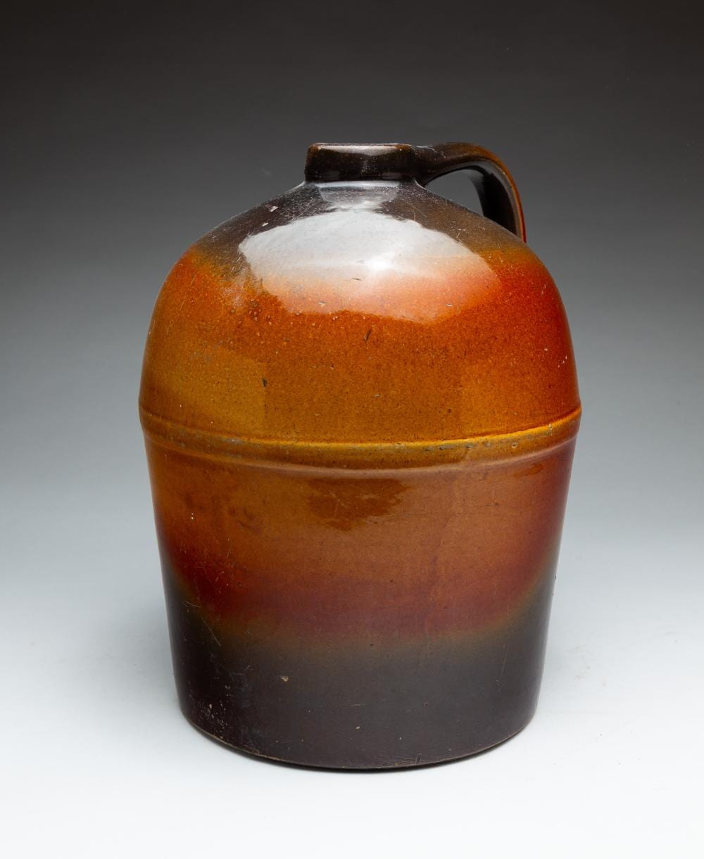 Brown glazed stoneware whiskey jug with arched handle and short spout lid.