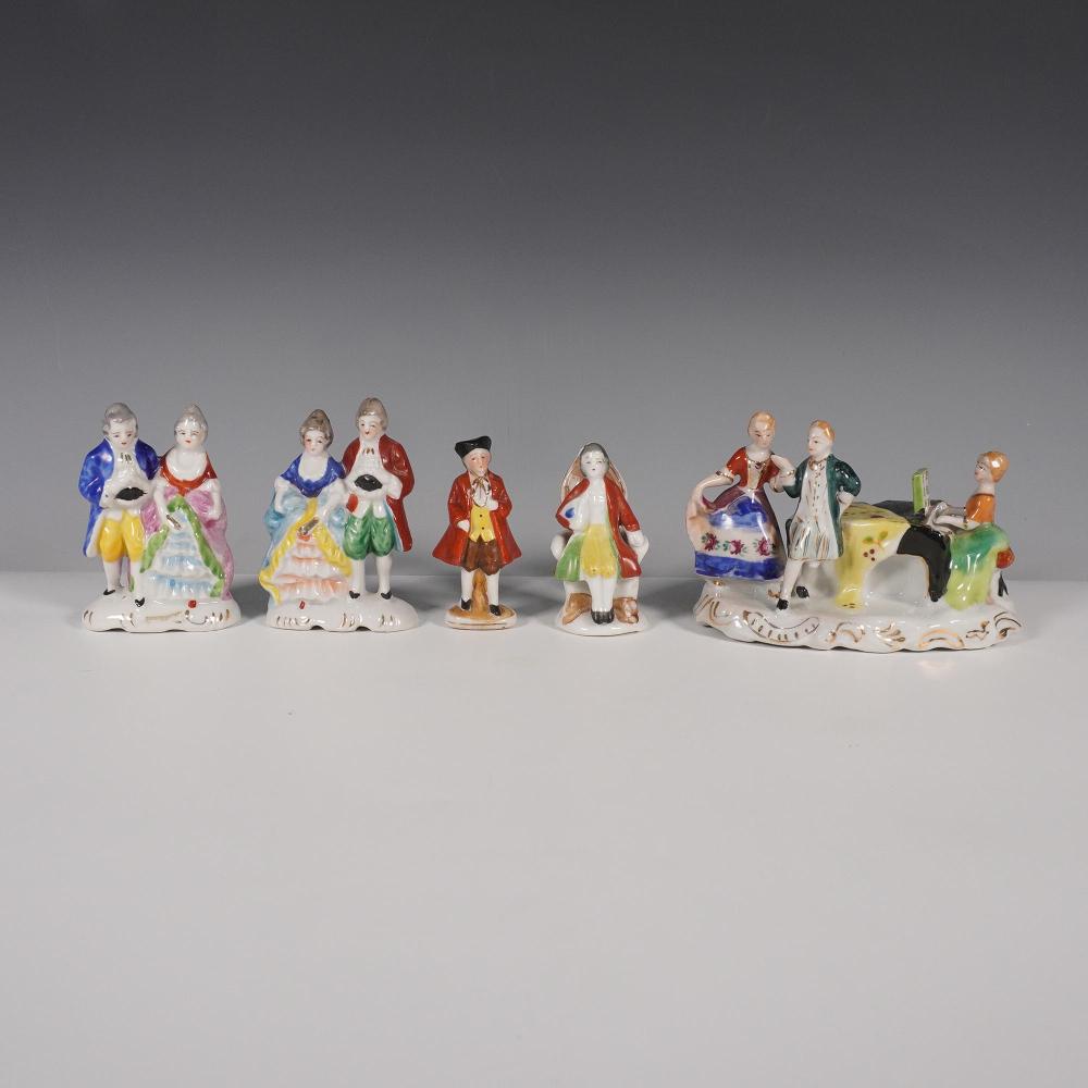 Five small painted porcelain figurines of people and children standing and sitting on a white display surface.