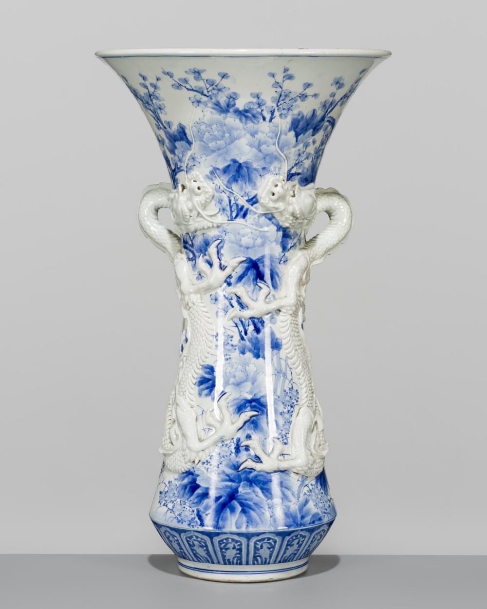 Blue-and-white porcelain vase with an flared rim and two molded dragon handles, decorated with floral and landscape-like scenes.