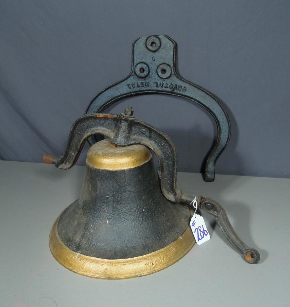 Cast iron bell with a brass-colored clapper and metal handle loop against a plain background.