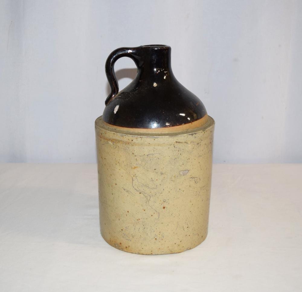 Stoneware jug with a black glazed top and a light tan body, shown standing against a plain background.