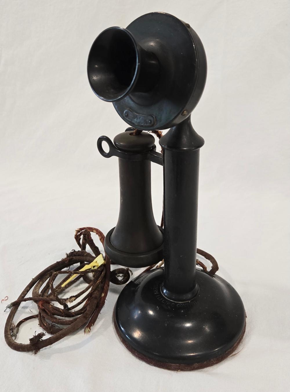 Black antique candlestick-style telephone with a small handpiece on a base, shown with tangled brown cord.