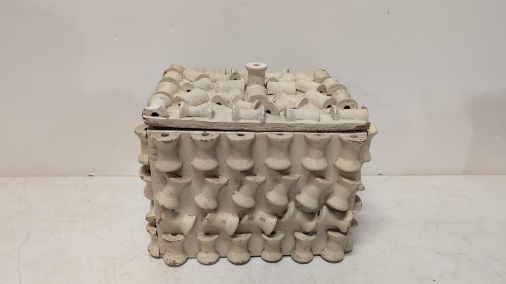 White folk art style sewing box with rows of rounded dowel-like pegs on the lid and front, on a plain background.
