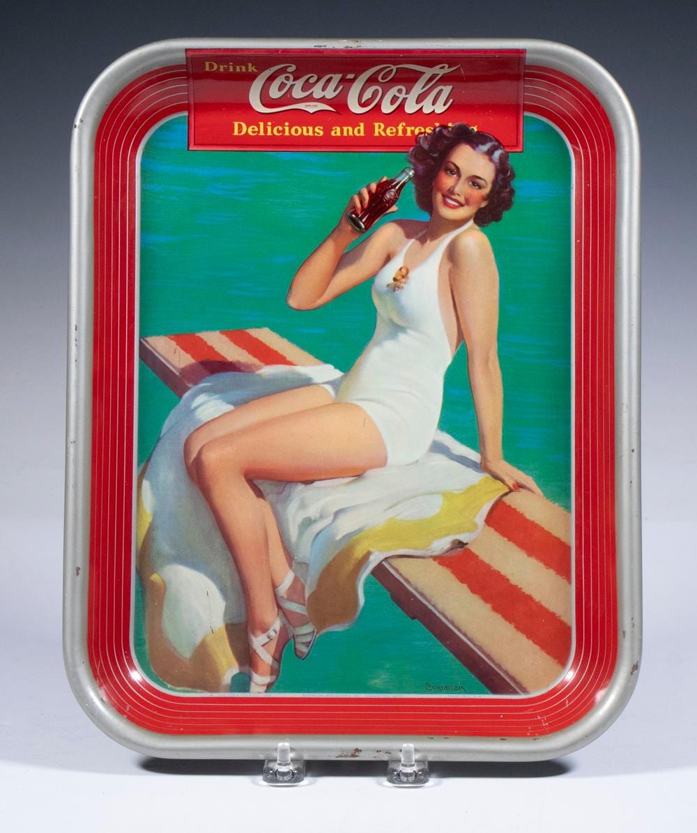 Vintage Coca-Cola serving tray with a pin-up style woman in a white swimsuit holding a bottle, shown in front of a beach scene and red logo panel.