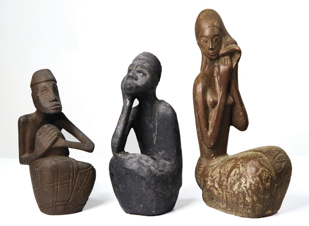 Three seated human figure sculptures on a white background, including one dark figure with hands on a body and two seated figures in bronze tones.