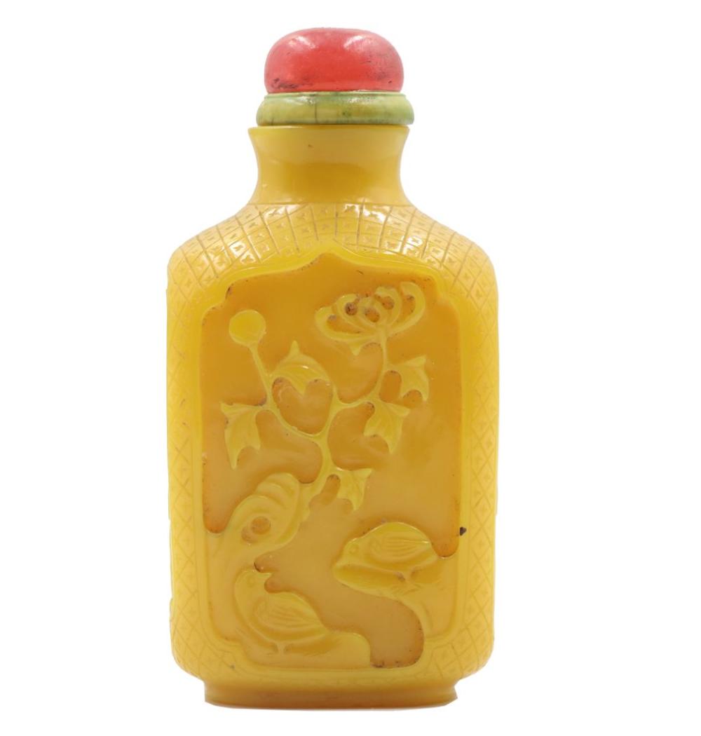 Yellow glass snuff bottle with a rounded red stopper and embossed decorative panels with animals and flowers.