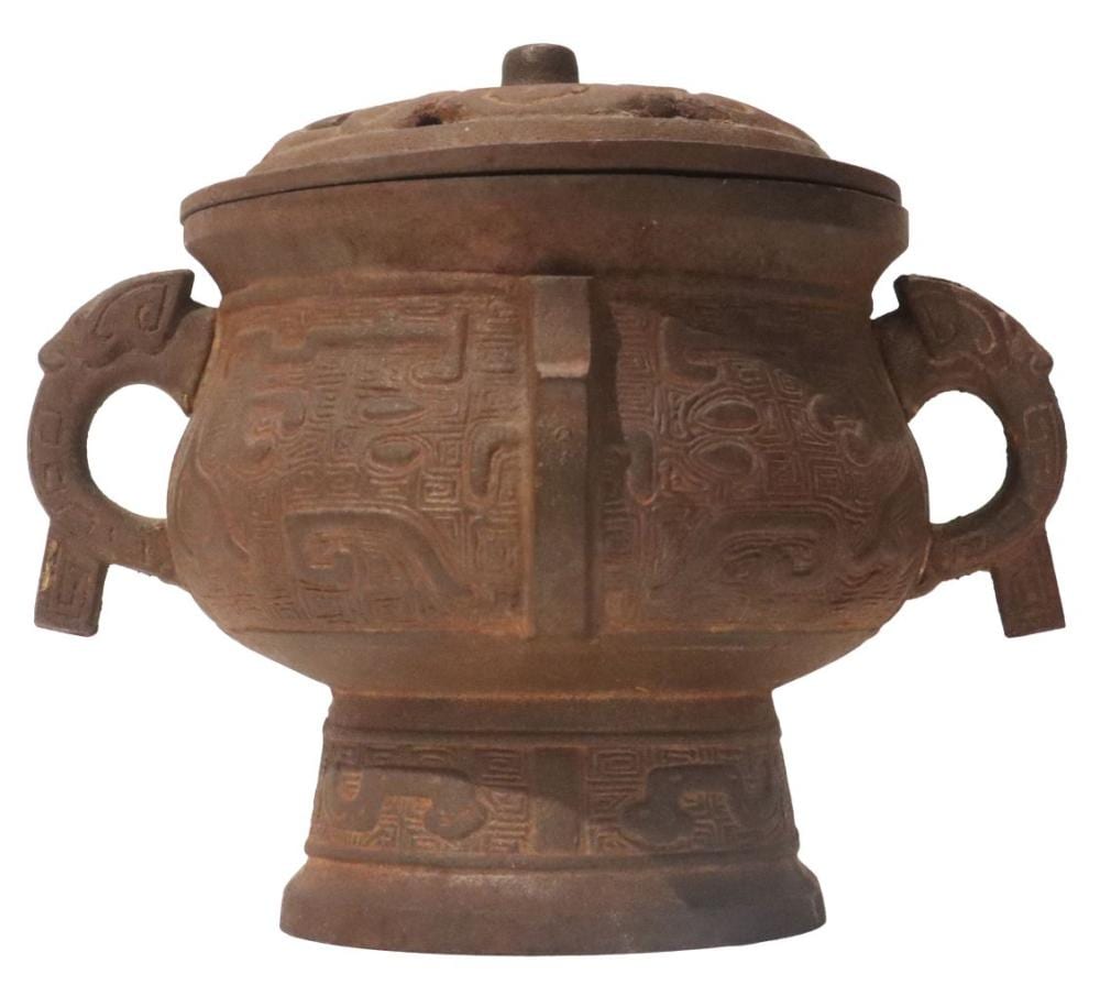 Brown bronze incense burner with a domed lid and two side loop handles, covered in raised geometric and animal-like relief patterns.