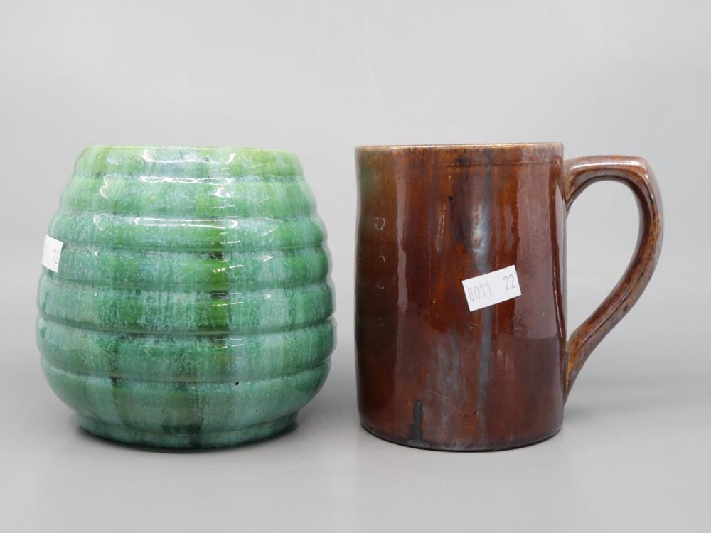 Two glazed ceramic vessels on a light background: a green beehive-style vase with horizontal bands and a brown handled mug or jug with a C-shaped handle.