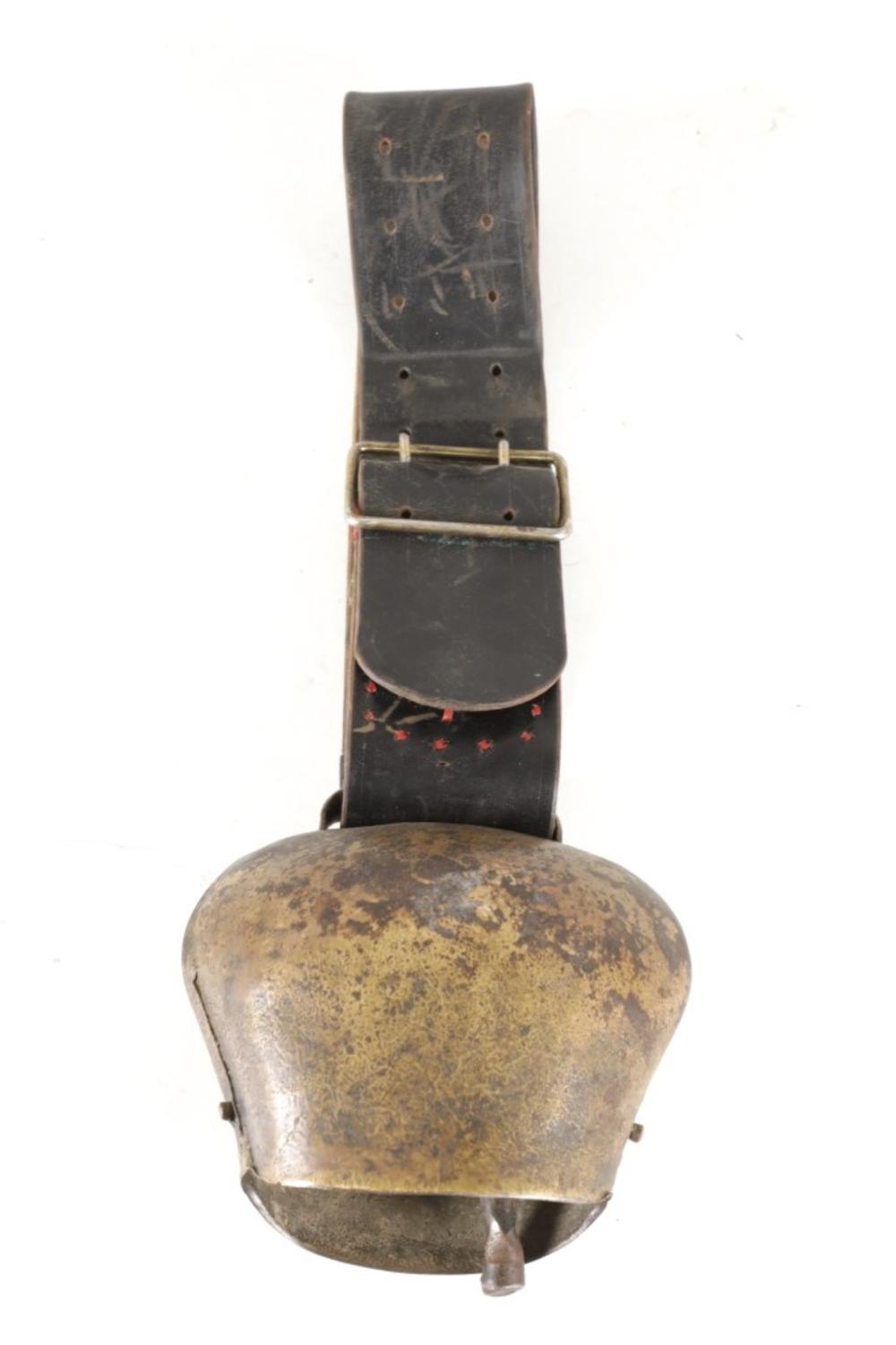 Antique-style metal cow bell with a worn leather strap and a black band decorated with small red markings.