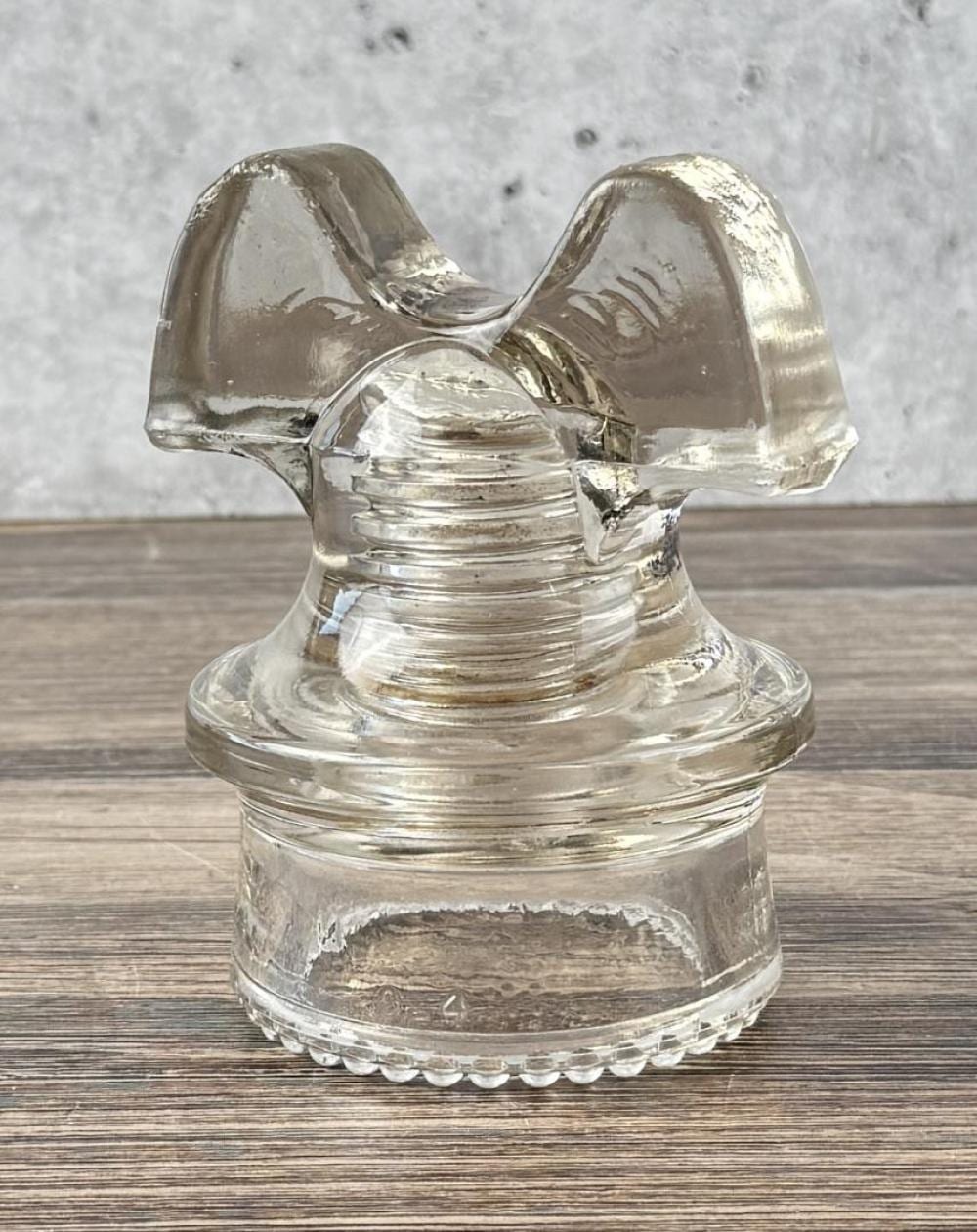 Clear glass insulator with a flared top and ribbed cylindrical base, photographed on a wooden surface.