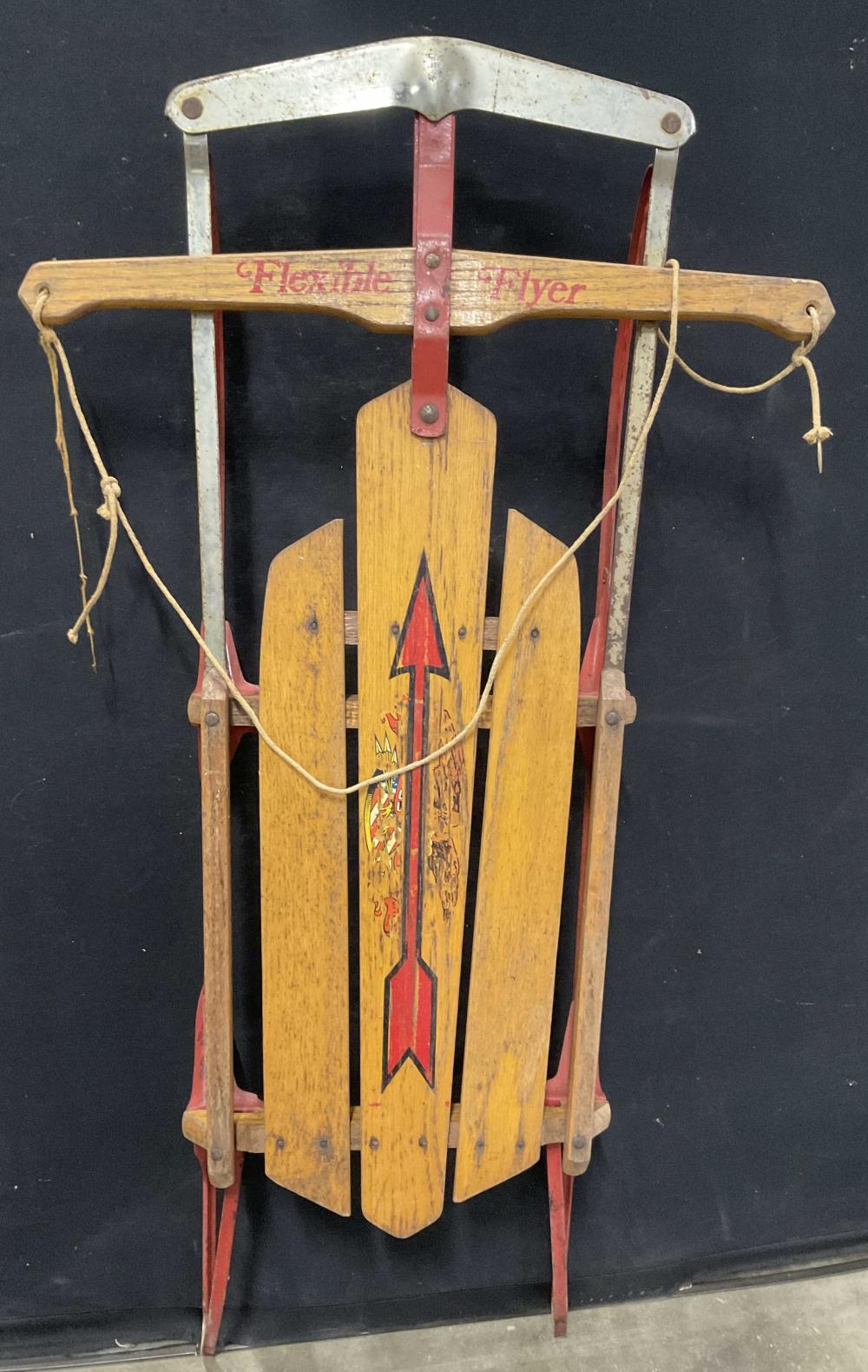 Vintage wooden and metal sled with red accents and a colorful arrow design on the front panel, photographed against a dark background.