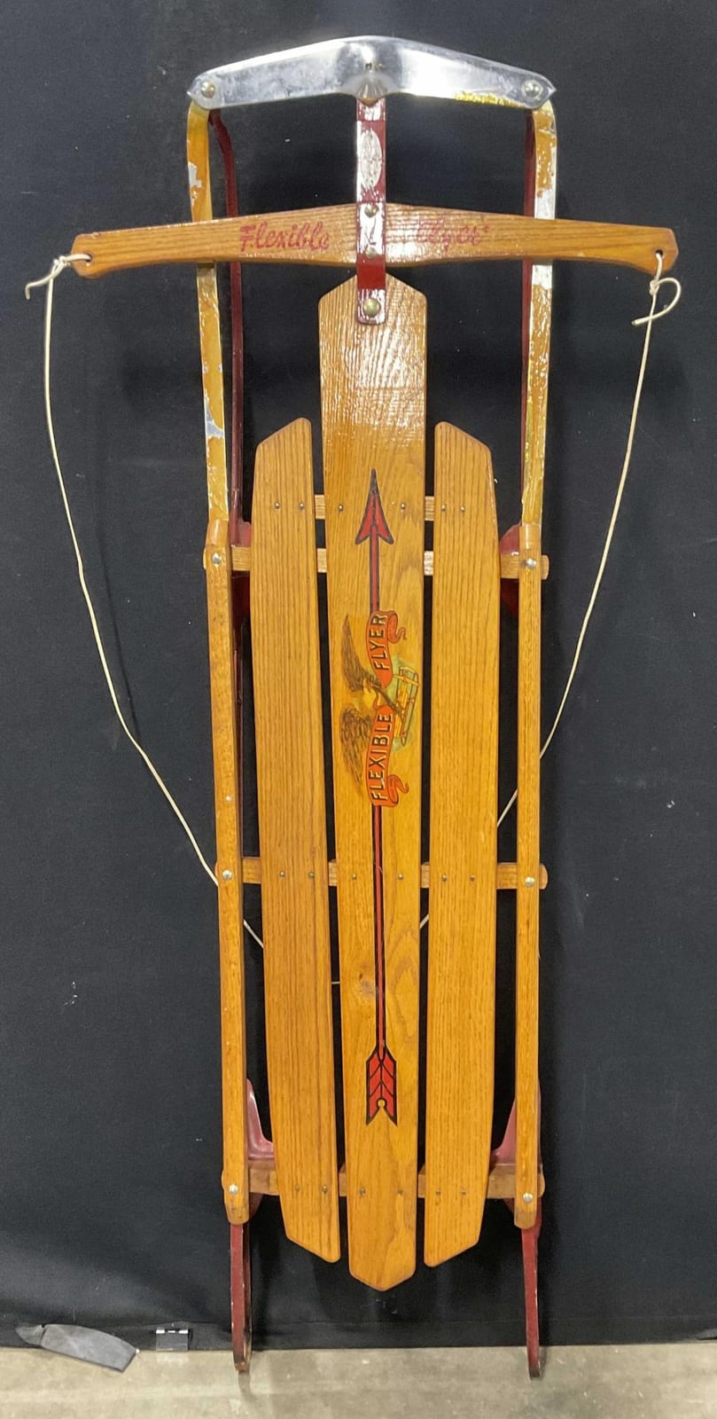 Wooden vintage sled with “Flexible” graphics, red-and-yellow front panel, and curved metal runners against a dark background.