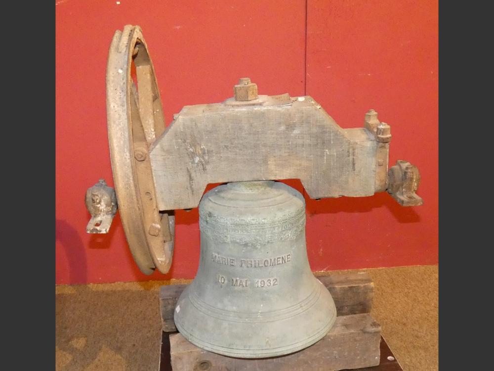 Antique cast iron bell with a wooden-and-metal mounting, shown against a red background, with raised lettering on the bell