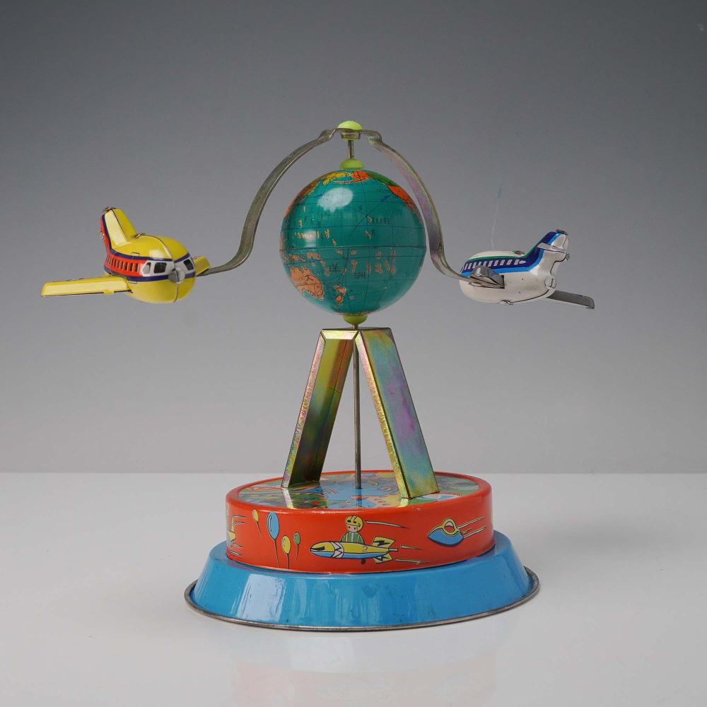Wind-up globe plane toy on a rotating platform, with a blue base and red outer ring showing cartoon figures and a globe in the center.