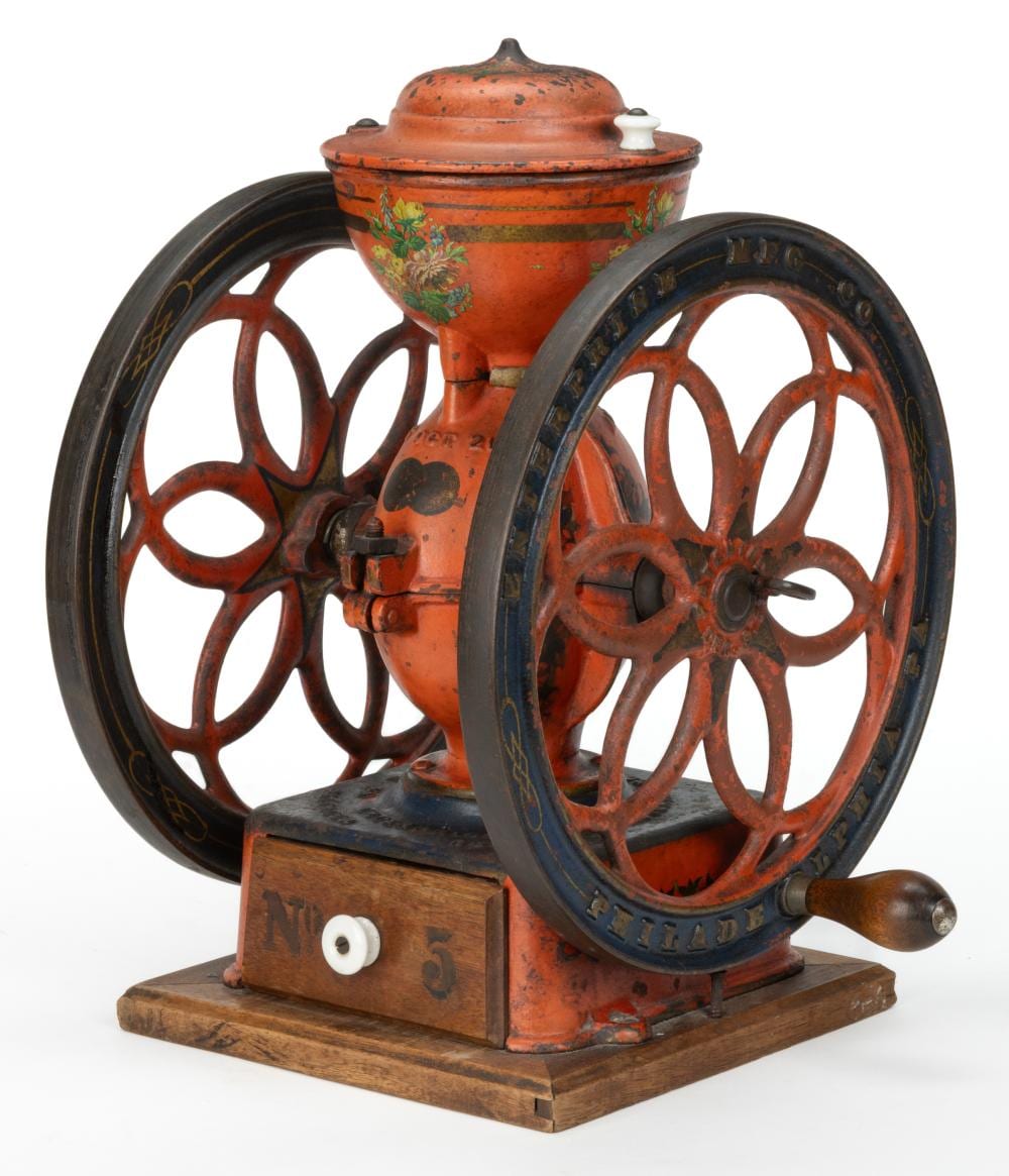 Cast-iron two-wheel hand coffee grinder with orange and black paint and a round hopper on top.