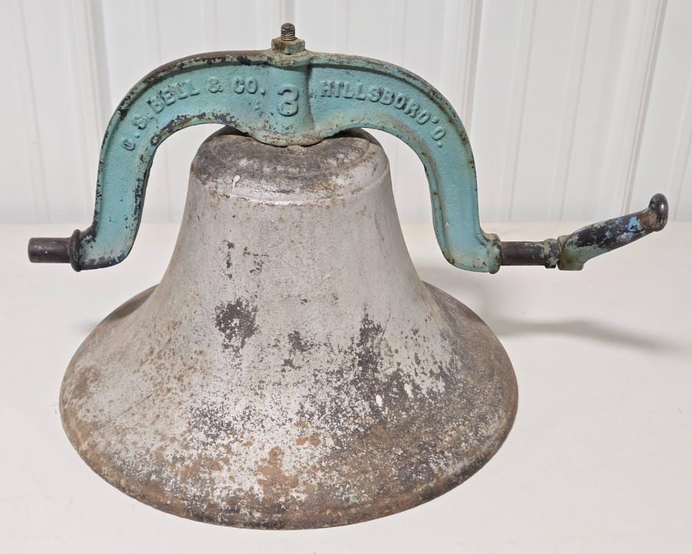 A large metal cast bell with a weathered gray surface and a light blue arched handle frame, shown on a white background.