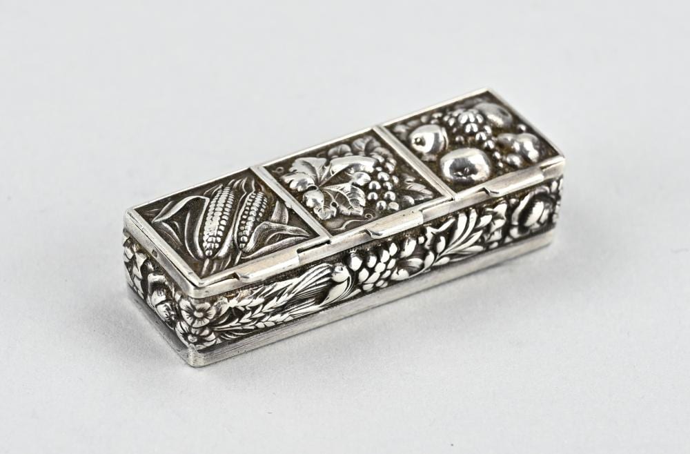 Metal pill box with hinged lid and engraved floral and scroll pattern, shown on a light background.