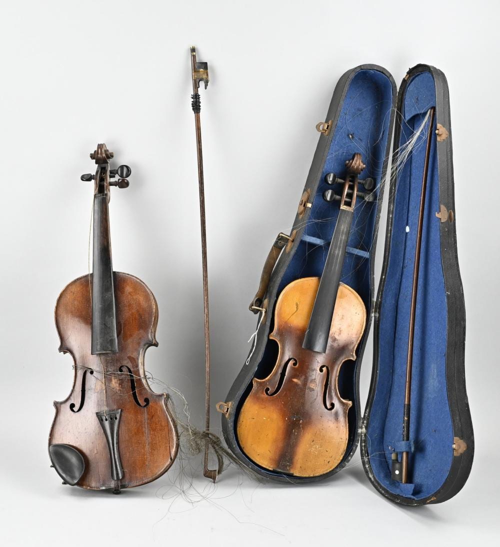 Two old violins shown side by side with bow and a blue case; one violin has strings and bridge visible.